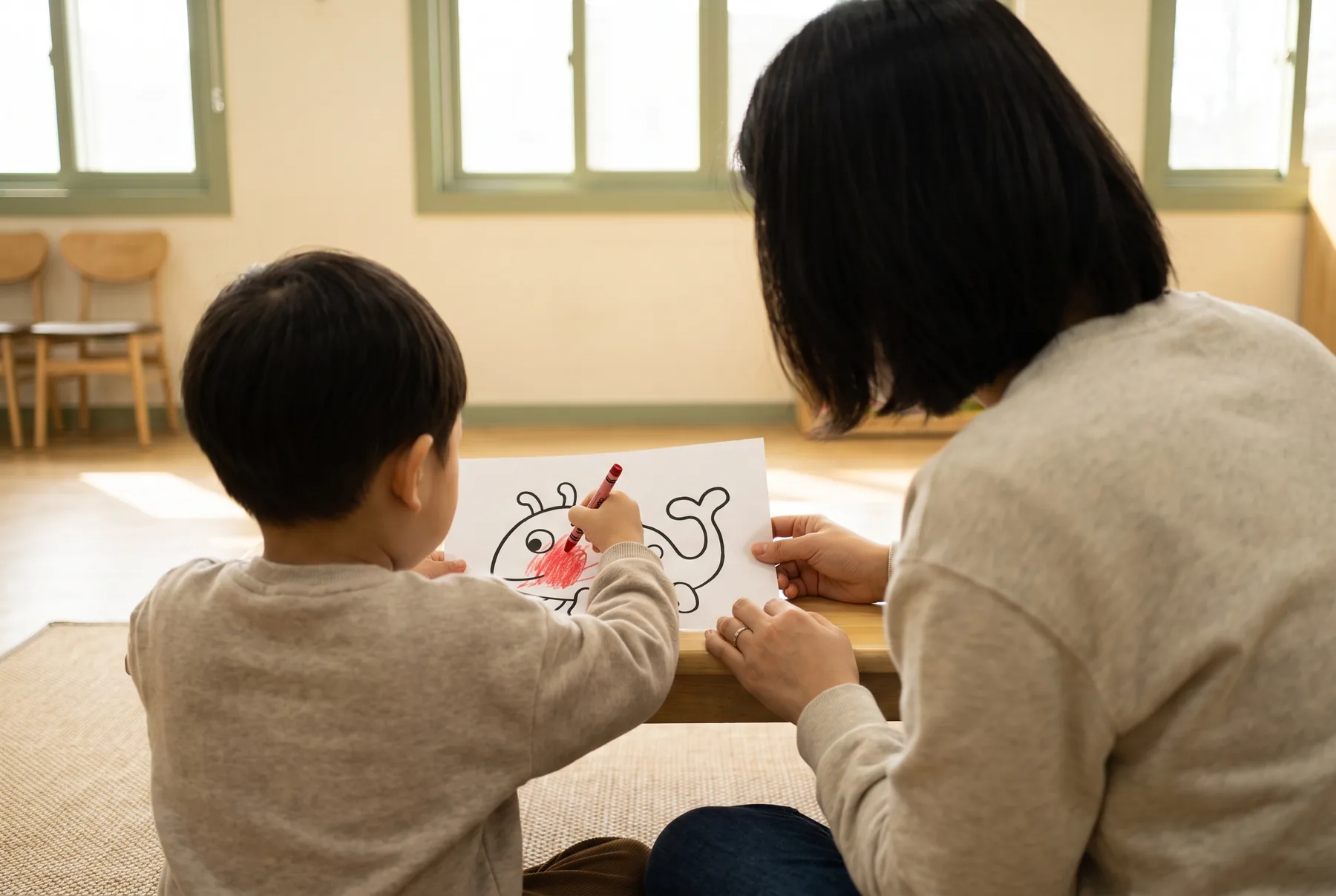 보호자와 아이가 함께 앉아 그림을 그리는 모습